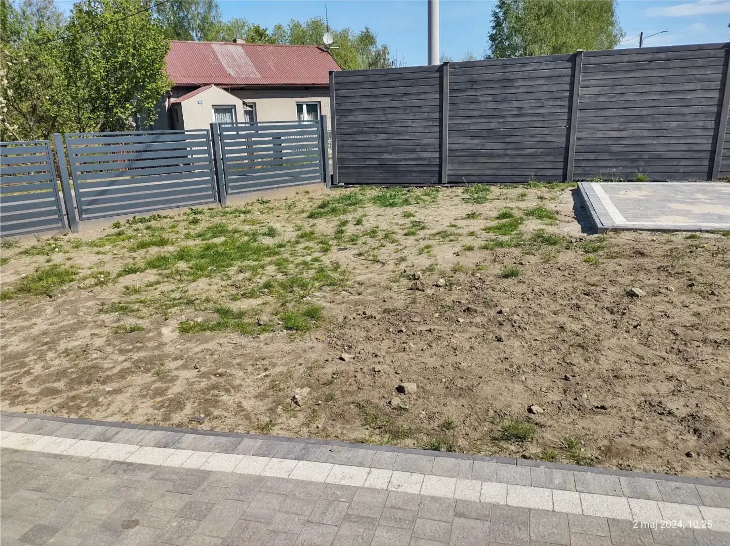 Teren przygotowany pod usługę Zakładanie trawników, z wyrównanym podłożem, resztkami trawy i panelowym ogrodzeniem