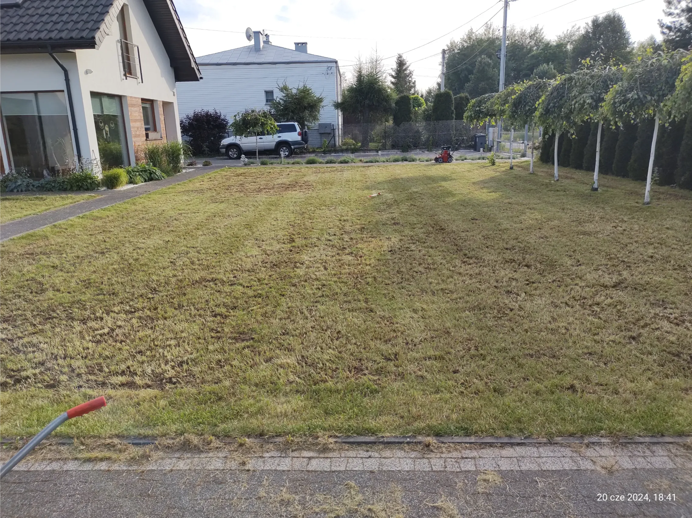 Koszenie trawy: świeżo skoszony trawnik przed domem z widoczną kosiarką i pergolą winorośli