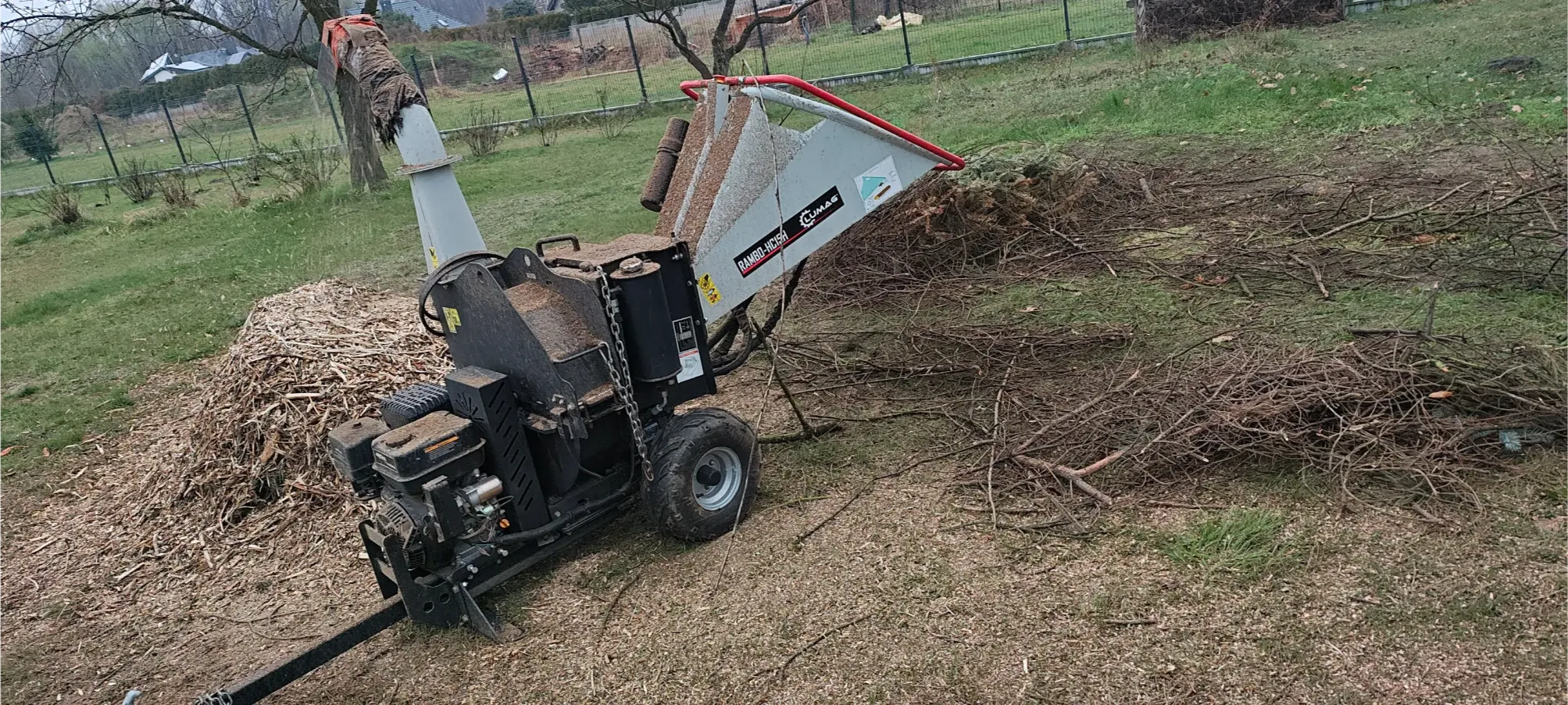 Spalinowy rębak do gałęzi z rozdrobnionymi wiórami drewna na trawniku, usługi rębakiem